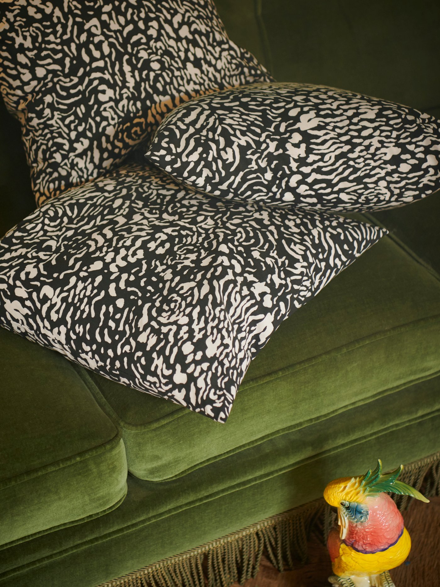 A bunch of GRIMHILD cushion covers featuring an abstract black and natural pattern placed in a green velvet sofa.