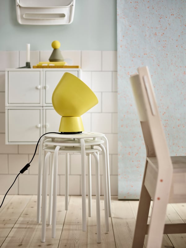 A stack of MARIUS white stools with a yellow table lamp on top.