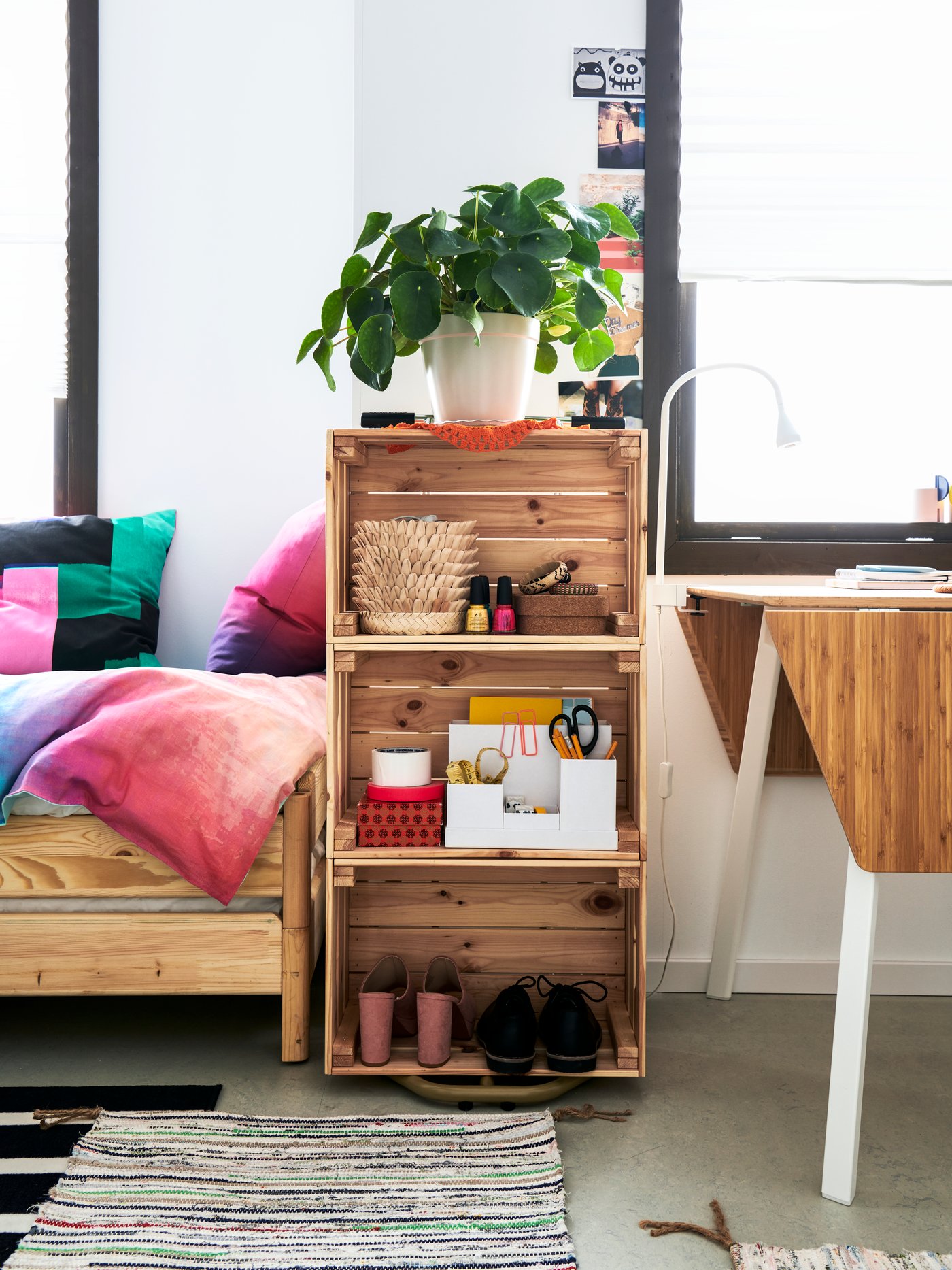 Sala de estar con un almacenamiento abierto con ollas, una planta en maceta y una caja, mesa abatible con lámpara de trabajo y una alfombra.