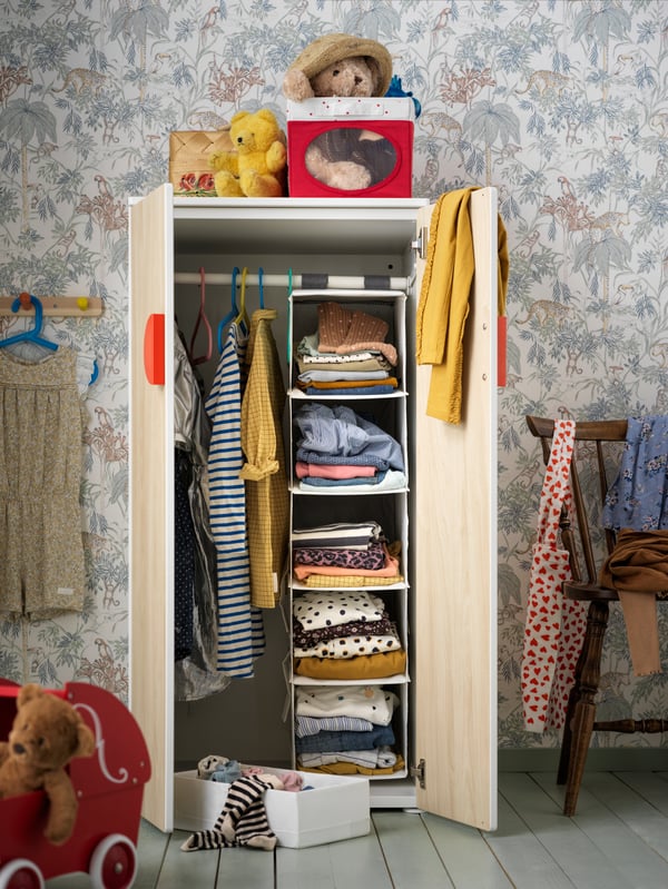 Es ist ein geöffneter Kleiderschrank in einem Kinderzimmer zu sehen. Darin ist Kleidung verwahrt.