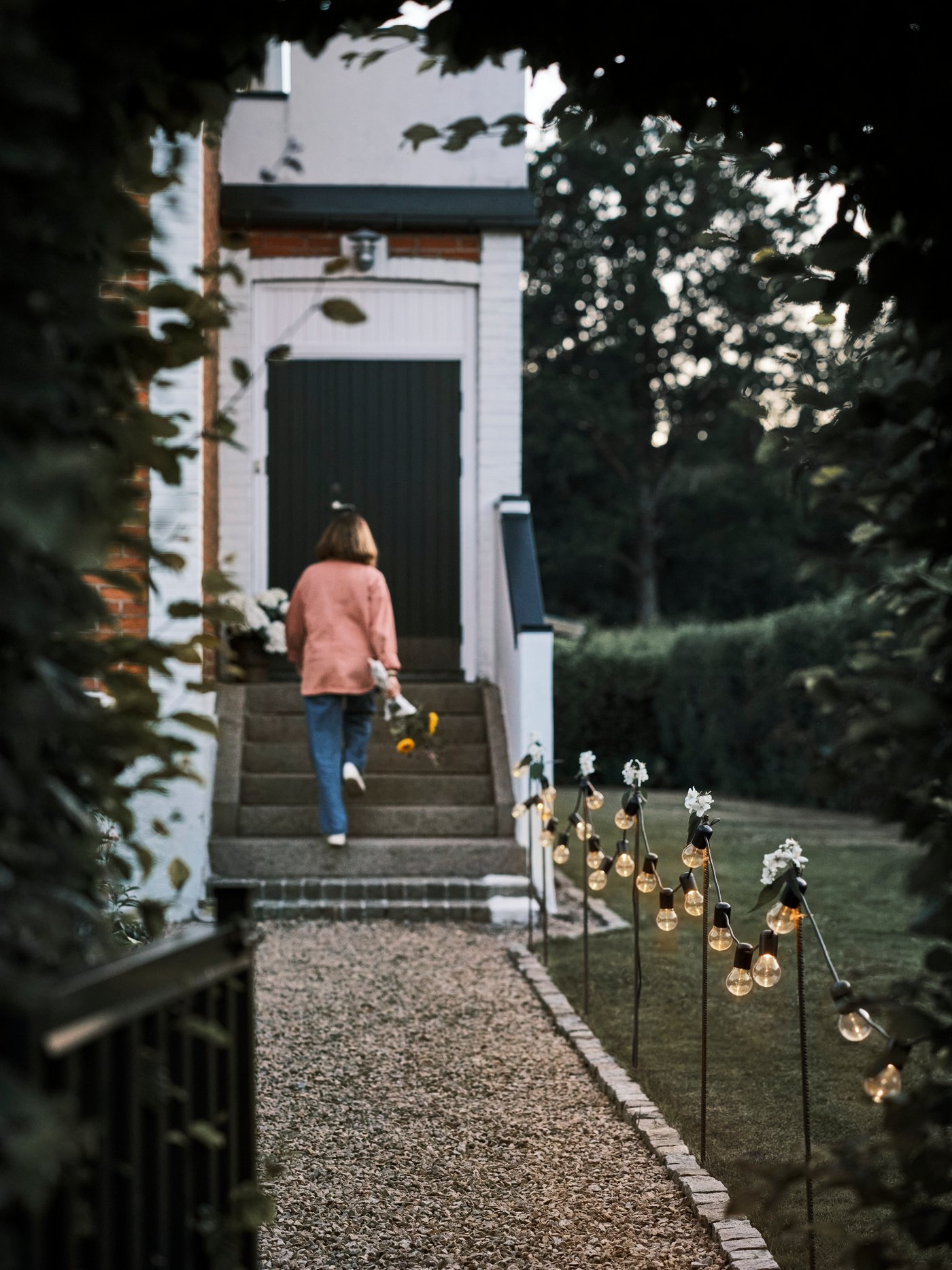 Crni SVARTRÅ LED lanci vise duž staze posute šljunkom koja vodi do kuće gde osoba hoda uz stepenice.