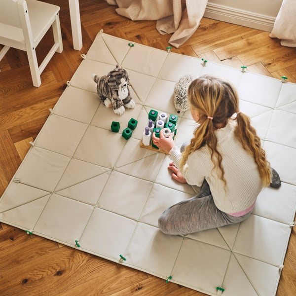 A child plays with a GREJSIMOJS board game on a GREJSIMOJS mat/storage box folded out to use as a mat.