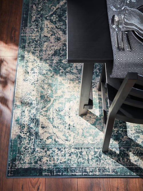 Overhead shot of a dining room with a chair and a table with multiple cutlery items and a tablecloth, set on an ornate rug.