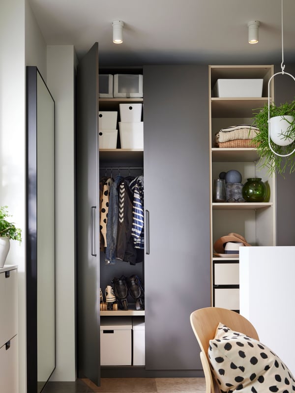 Two white NYMÅNE ceiling spots shine down in front of a dark grey PAX/FORSAND wardrobe with an open door.