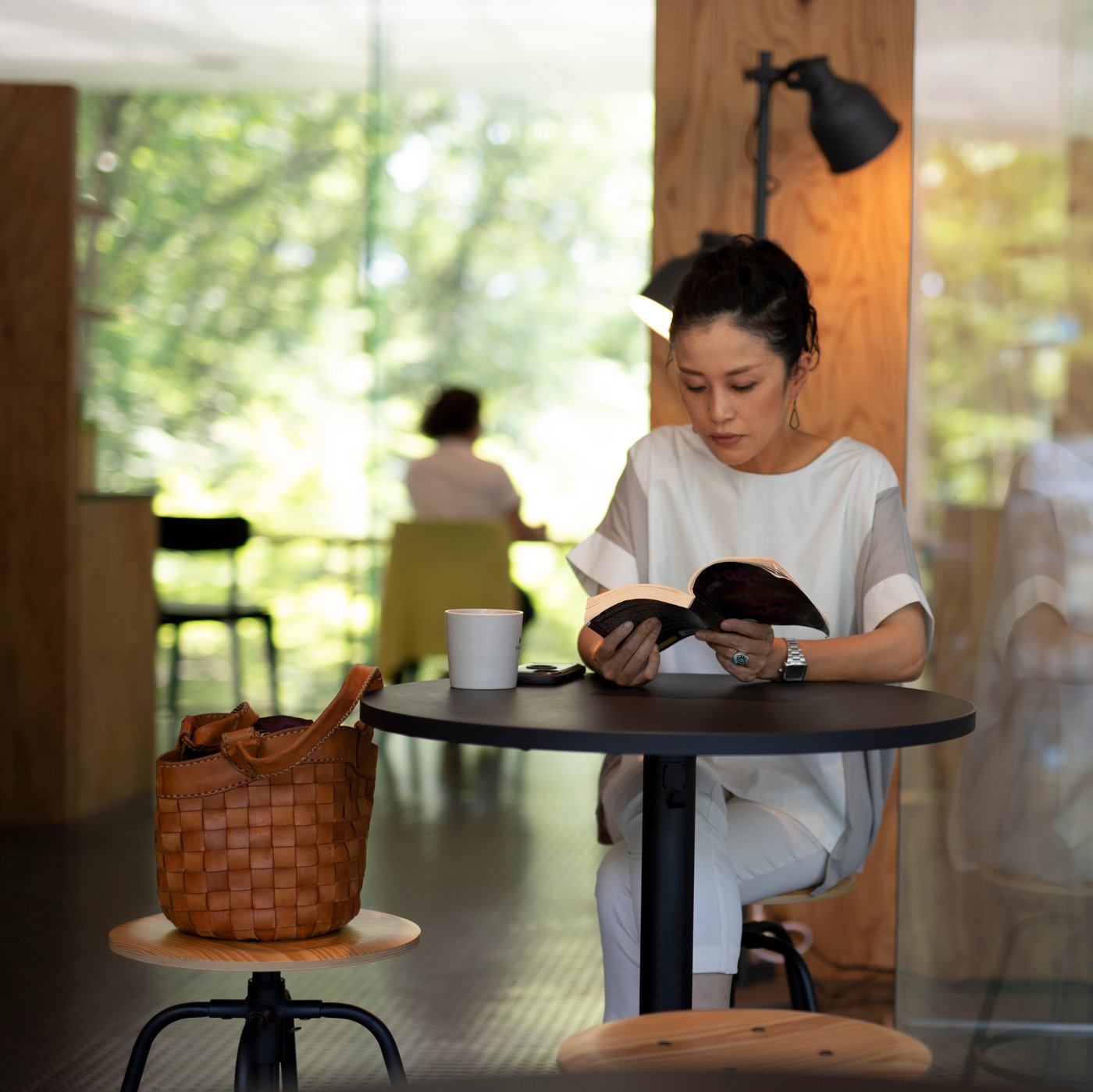 zu sehen ist eine dame auf einem hocker, an einem hohen steh Tisch die gerade ein Buch liest.