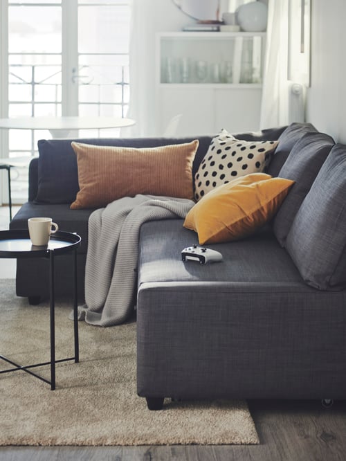 Living room featuring a corner sofa bed with storage with multiple cushions and a throw. A tray table is next to the sofa.