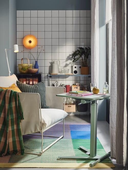 A living room with a MITTZON laptop table with castors, an outdoor armchair with cushions and a throw, and a shelving unit.