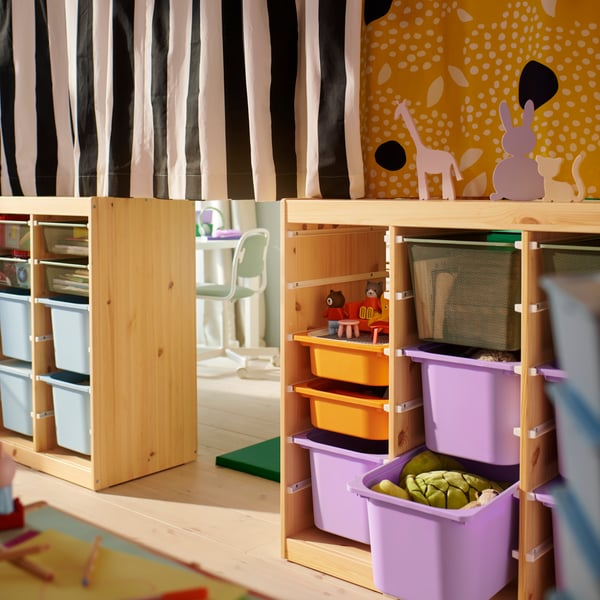 Twee TROFAST kamerverdelers met elk een ander gordijn met patroon dat over de bovenkant is getrokken in een gedeelde kinderslaapkamer.