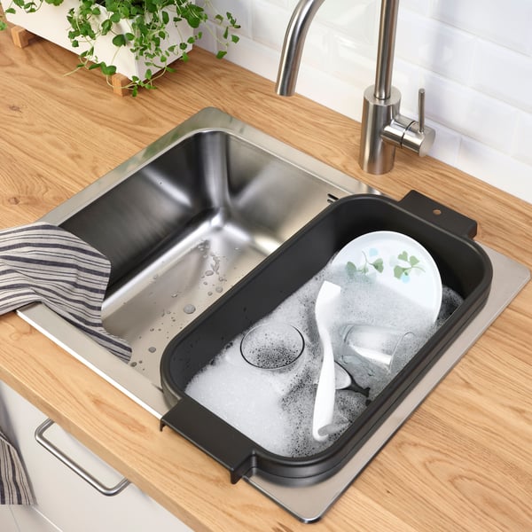 A close-up view of a modern kitchen sink with a double basin, set against dark cabinetry. Above the sink is a window that offers a view of a serene, hilly landscape. The scene is interesting as it combines interior design elements with an idyllic outdoor setting, suggesting comfort and tranquility within the home environment.
