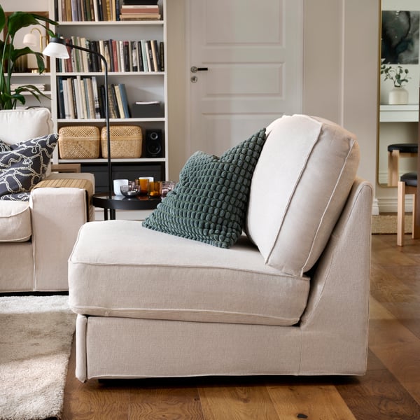 A light beige KIVIK 1-seat sofa-bed is positioned alongside a matching armchair in a cosy living room with bookshelves.