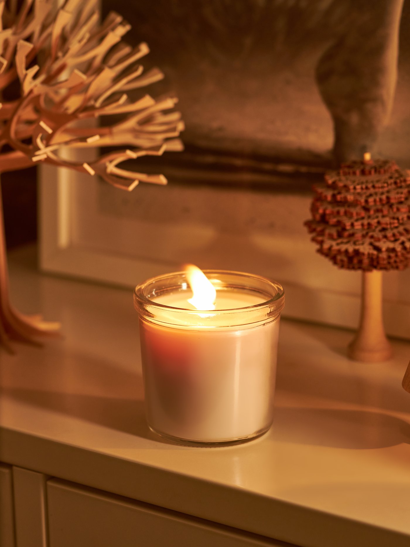 El borde de una ventana con flores secas y una vela blanca encendida.