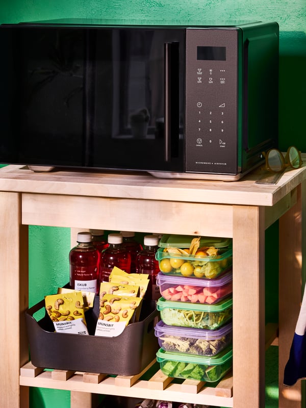 Freestanding GÅTEBO microwave oven/air fryer, a stack of purple and green PRUTA sandwich containers and ISKUB cashew nuts.