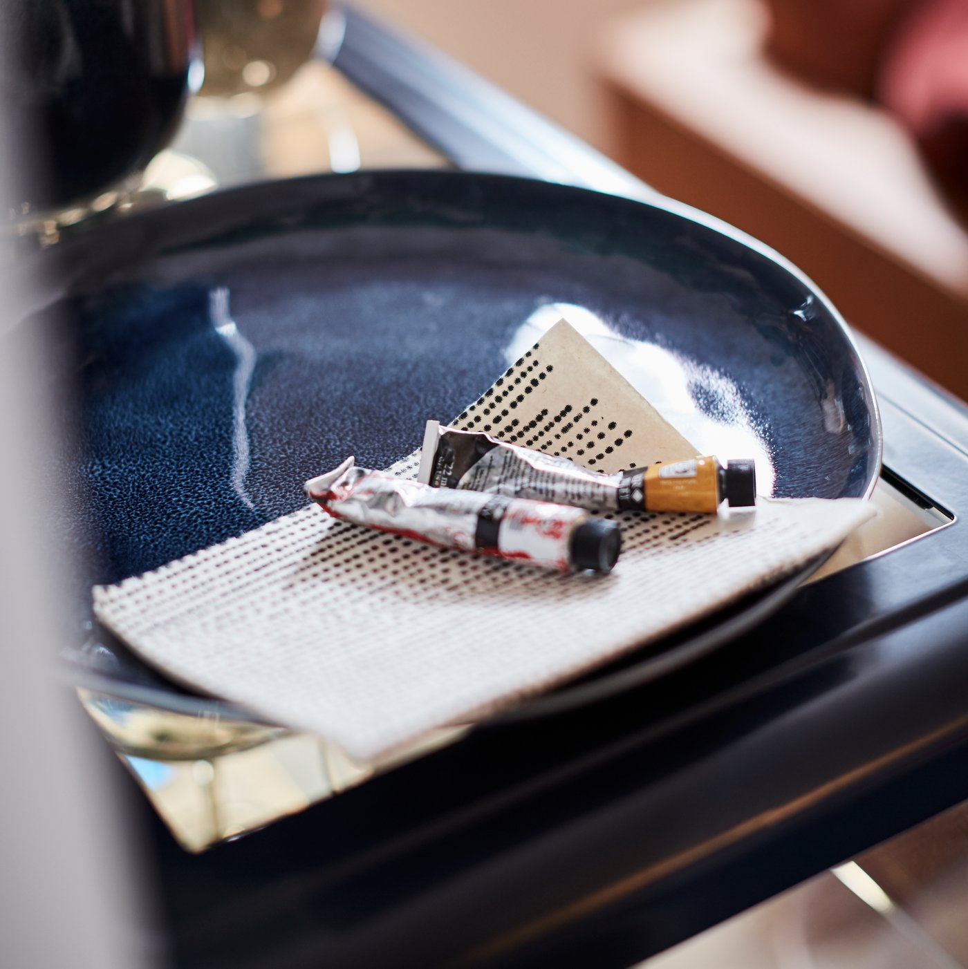 صورة مقربة لأنابيب ألوان مائية وورقة في صحن ERTAPPAD باللون الأزرق على طاولة في الزاوية.