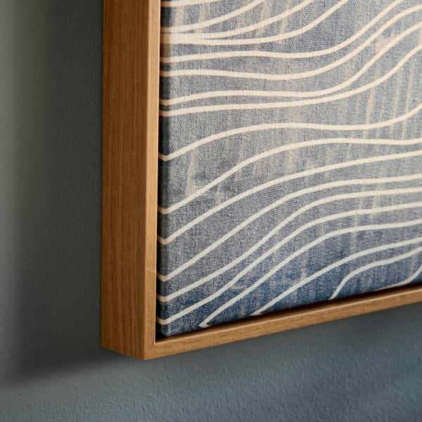 Gros plan sur une image BLODFLÄDER aux motifs bleus et blancs, encadrée dans un cadre en bois naturel, mettant en valeur ses lignes douces et fluides.