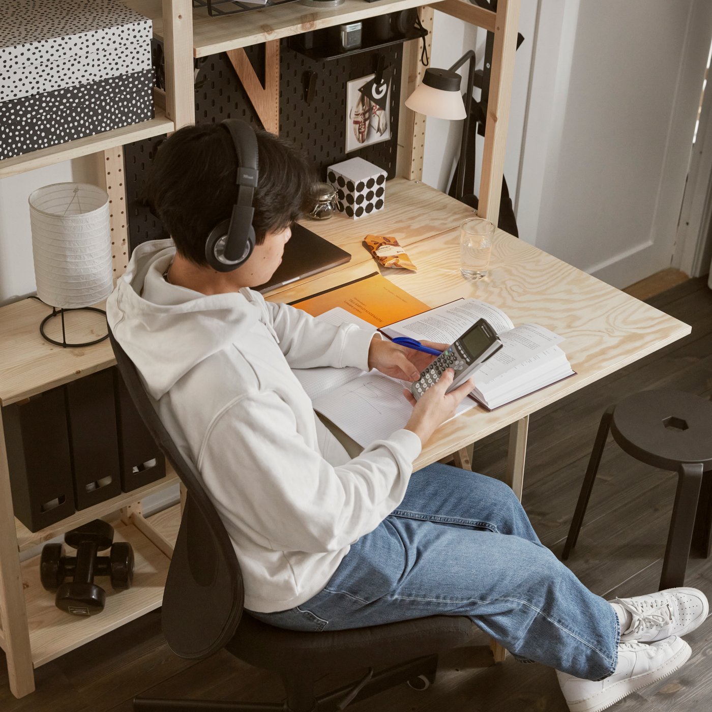 Eine Person studiert mit Büchern auf einem schwarzen Schreibtischstuhl an einem IVAR-Klapptisch, der an einem IVAR-Regal befestigt ist, alles aus Kiefernholz.