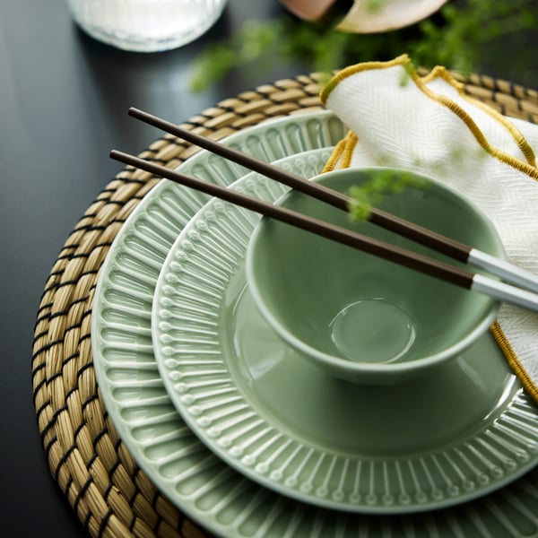 A STRIMMIG bowl with chopsticks laid on top stands on a STRIMMIG side plate and plate with decorative edges.