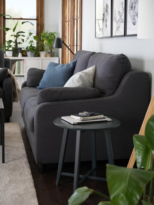 En antracitgrå 3-sists soffa bredvid ett runt sidobord.