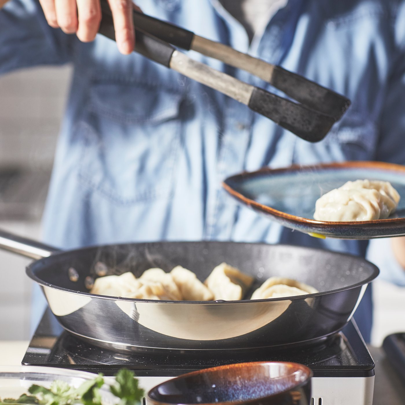 En person tager mad fra en stegepande med en tang.