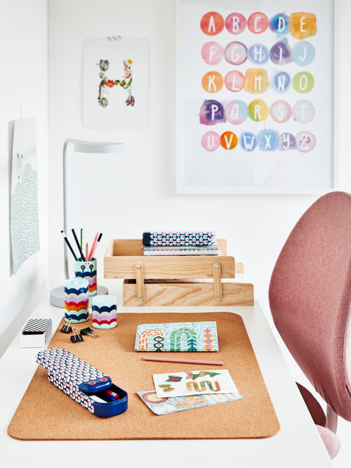 Workspace with a white surface that has a desk pad with a letter tray, pencil case, decoration boxes, and table lamp.