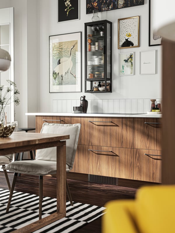 A kitchen with TISTORP fronts with a brown walnut effect and a MOSSJÖN wall cabinet with shelves and glass door.