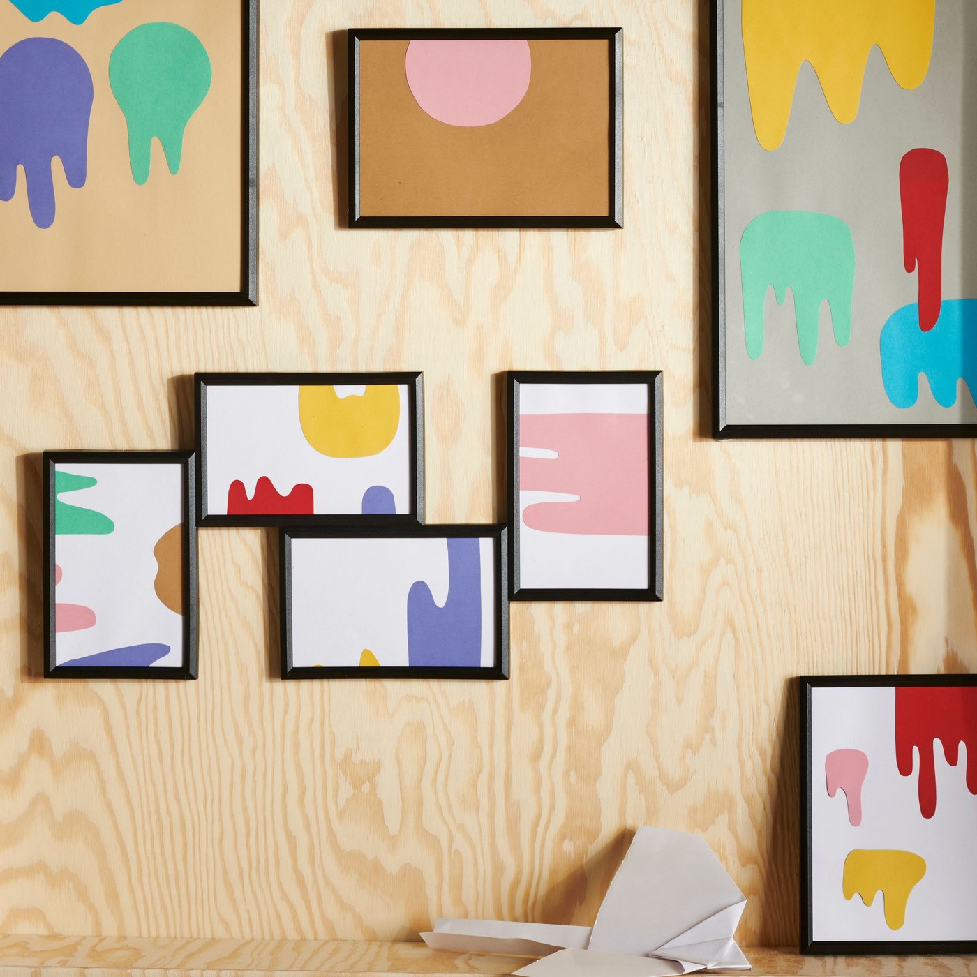 Wooden wall with multiple YLLEVAD frames containing abstract photos, and a BAJK alarm clock placed below.