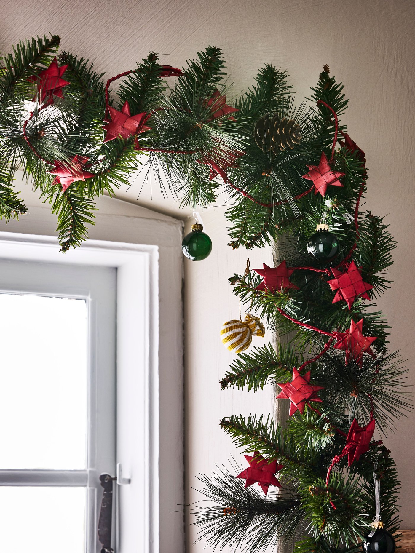 Una guirnalda de pino artificial VINTERFINT contorneando una centana con decoracines de estrellas rojas.