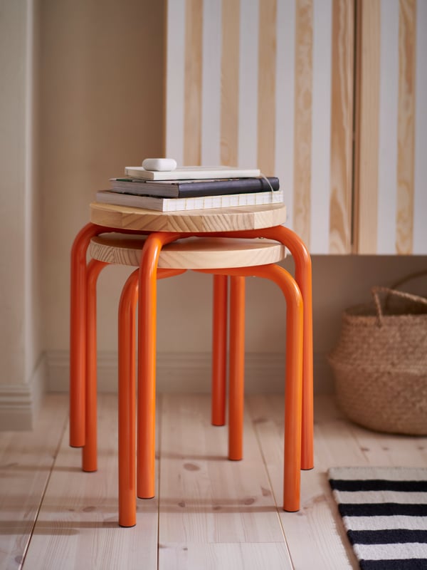 An orange/pine DOMSTEN stool with some books on top of it is stacked on top of another identical stool.