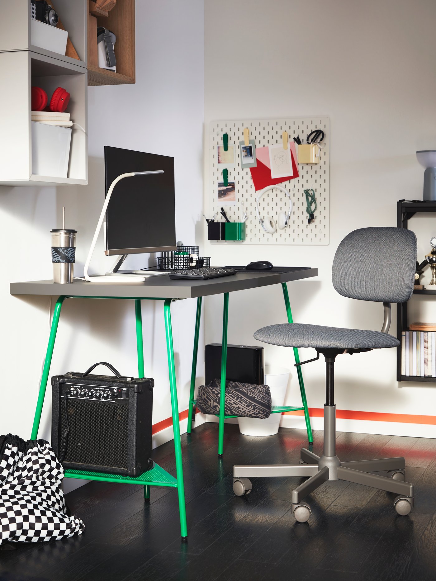 Tablero de escritorio LAGKAPTEN color gris, con caballetes metálicos TILLSLAG color verde. Sobre el escritorio hay un computador, una lámpara y un teclado. En la base del caballete se ve un amplificador de instrumento musical.