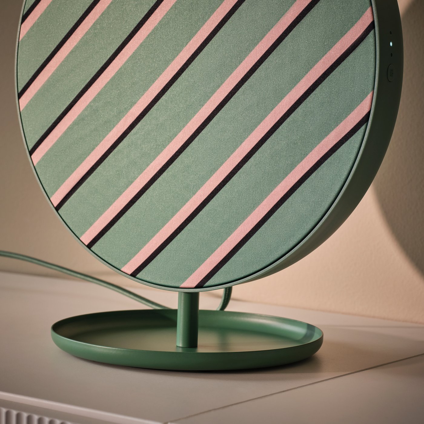 En grøn SOLSKYDD Bluetooth-højttaler med stribet design monteret på sit stativ, placeret på en overflade ved en væg.