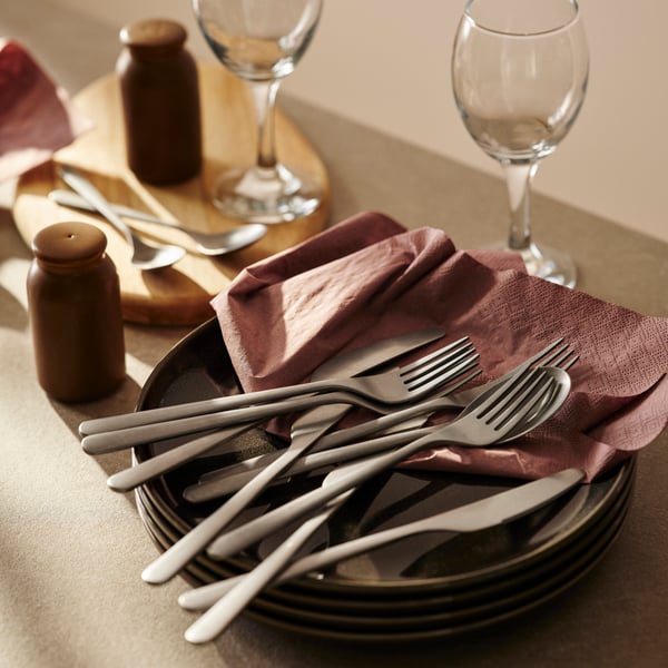 Stainless steel cutlery on a stack of plates with napkins.