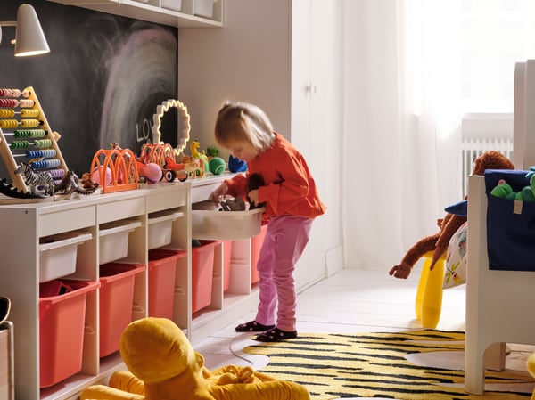 A children’s room with a long storage combination along the wall and a little girl looking for something in a drawer.