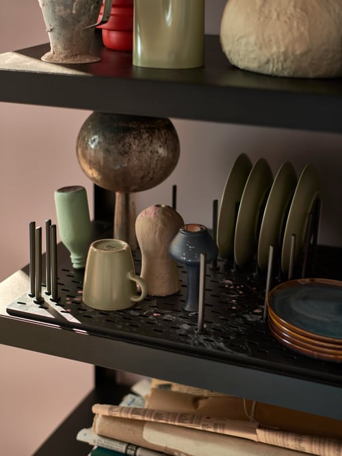 Un prim-plan cu un organizator de pegboard pe un raft cu mai multe farfurii, căni și alte obiecte din ceramică.