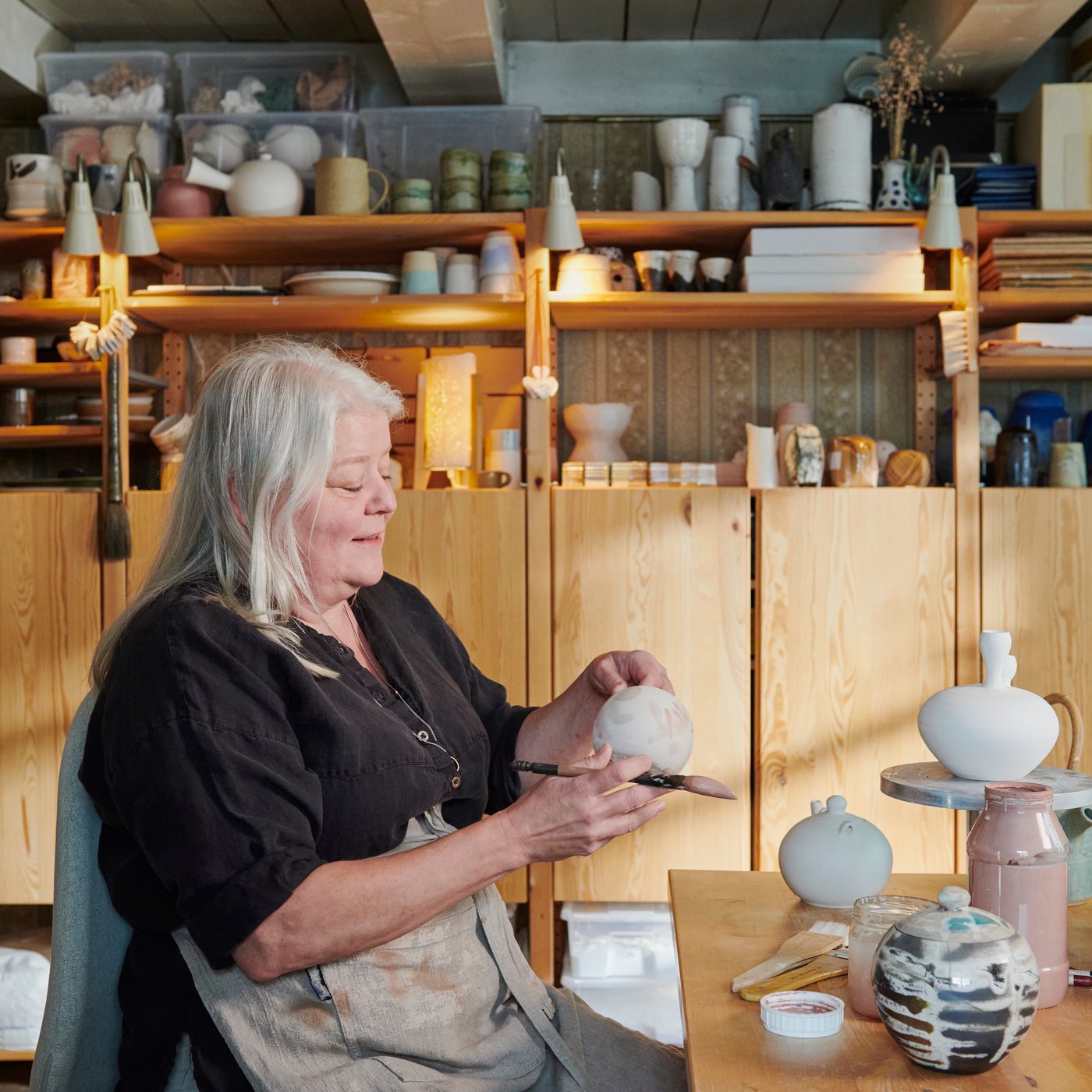 Wooden IVAR cabinets and shelves holding ceramics, jars and supplies in a pottery hobby space.				