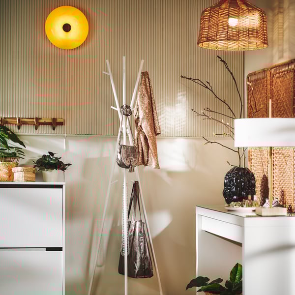 A white EKRAR hat and coat stand by a BISSA shoe cabinet holds various items with a round orange VARMBLIXT wall lamp above.