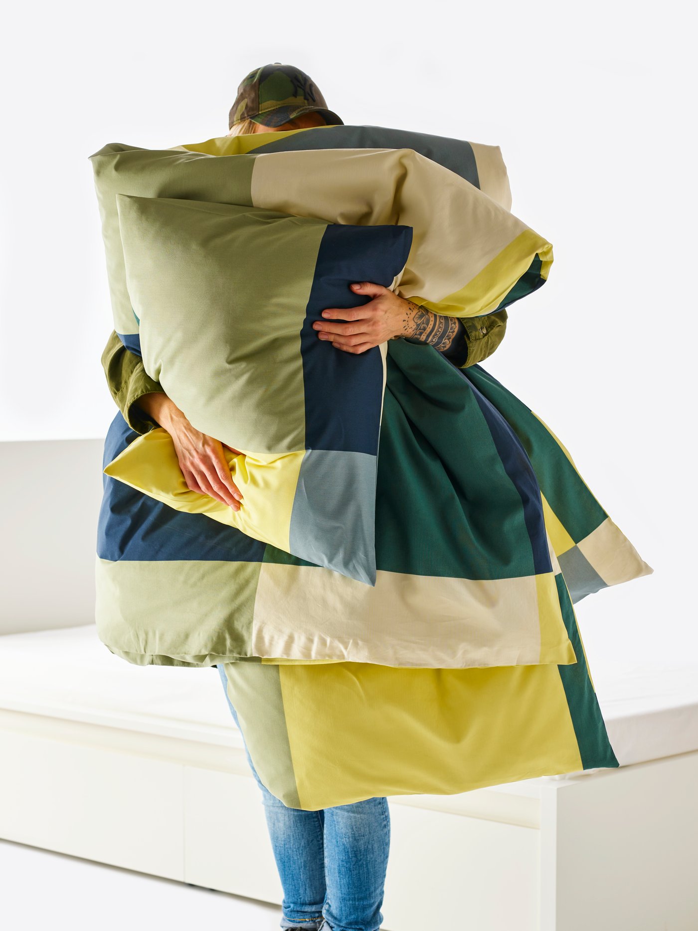 Un dormitorio con una persona sosteniendo una funda nórdica y funda de almohada BRUNKRISSLA de varios colores.