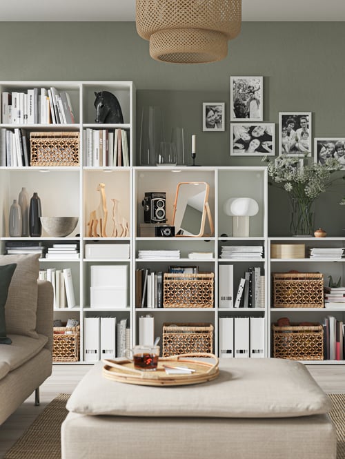 A white rectangular shelving combination containing several storage baskets, a lamp, a mirror, magazines, and a ceramic bowl.