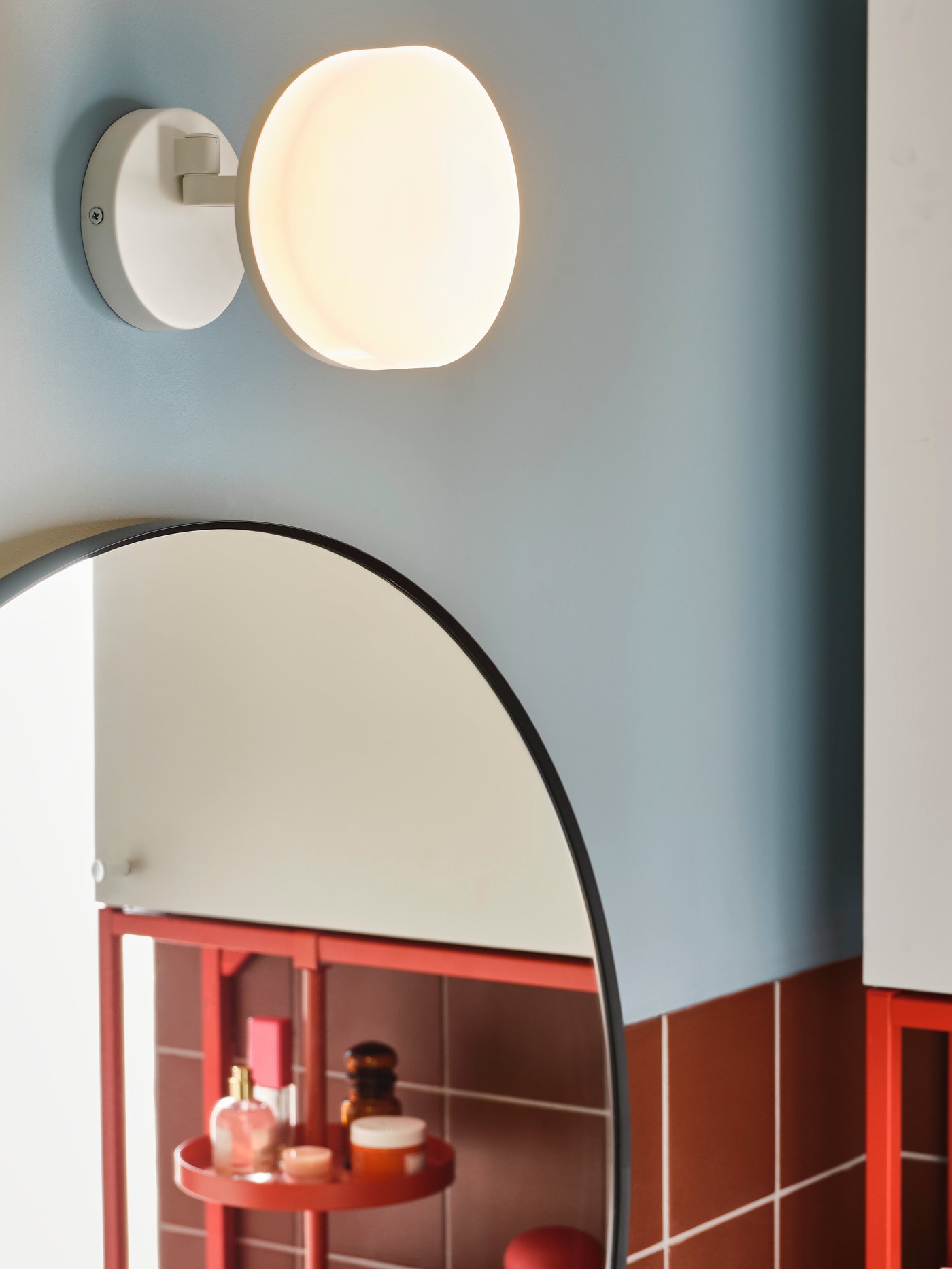 A white wall lamp with swing arm is wall-mounted above a round mirror in a bathroom.
