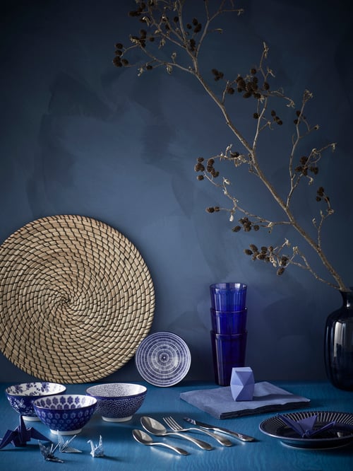 Blue and white ENTUSIASM bowls on a blue surface with blue glasses, napkins, plate and origami, cutlery and place mat.