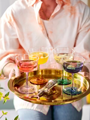 Personne tenant un plateau doré avec des boissons colorées dans des verres assortis.