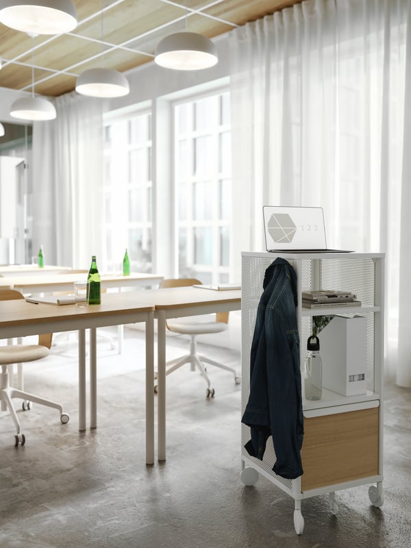 A white storage unit on castors used as a presentation stand in a conference room. A jacket hangs on a hook on its side.
