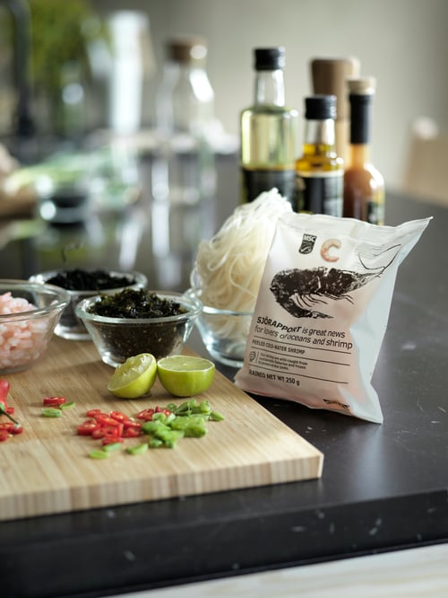 Bucătărie cu dulap de bază, blat de lucru, bloc de măcelărie, boluri de servire, o pungă de creveți decojiți, ingrediente de gătit, condimente.