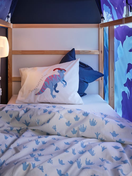 Close-up of a white duvet cover and pillowcase with dinosaur imprint placed on a reversible bed, and a bed tent to the side.
