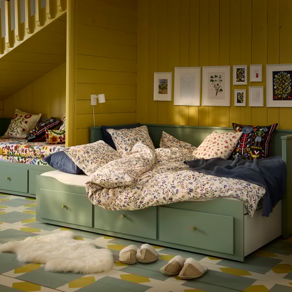 A grey-green HEMNES day-bed frame with 3 drawers featuring floral bedding and cushions in a cosy, inviting setting.