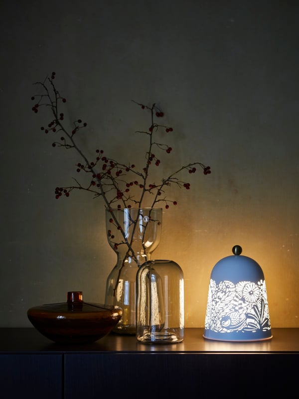 A tall decorative vase with autumn foliage, two short vases and a nature-inspired table lamp set on a sideboard.