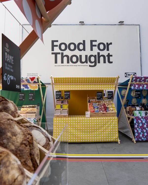 Stand colorati in stile mercato con esposizione di prodotti alimentari sotto l’insegna “Food For Thought”.