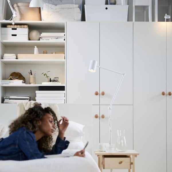 Iemand ligt te ontspannen op een bed in een multifunctionele woonruimte met witte LASTARE-kasten en -planken.