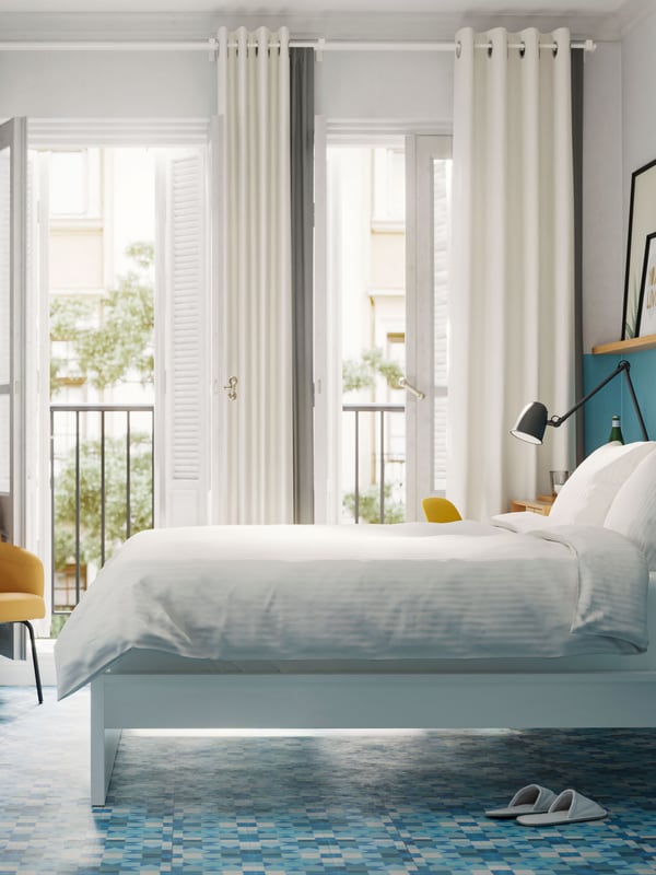 A MALM bed frame with NATTJASMIN duvet cover and pillowcases is near open balcony doors in a blue and white hotel room.