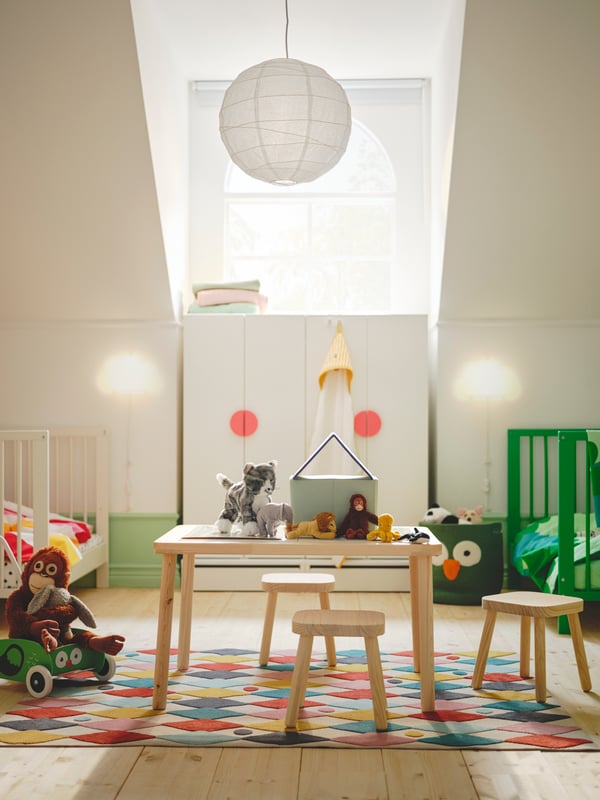 A white SMÅSTAD/UPPFÖRA wardrobe with light red handles behind a FLISAT children’s table and three stools on a BUSENKEL rug.