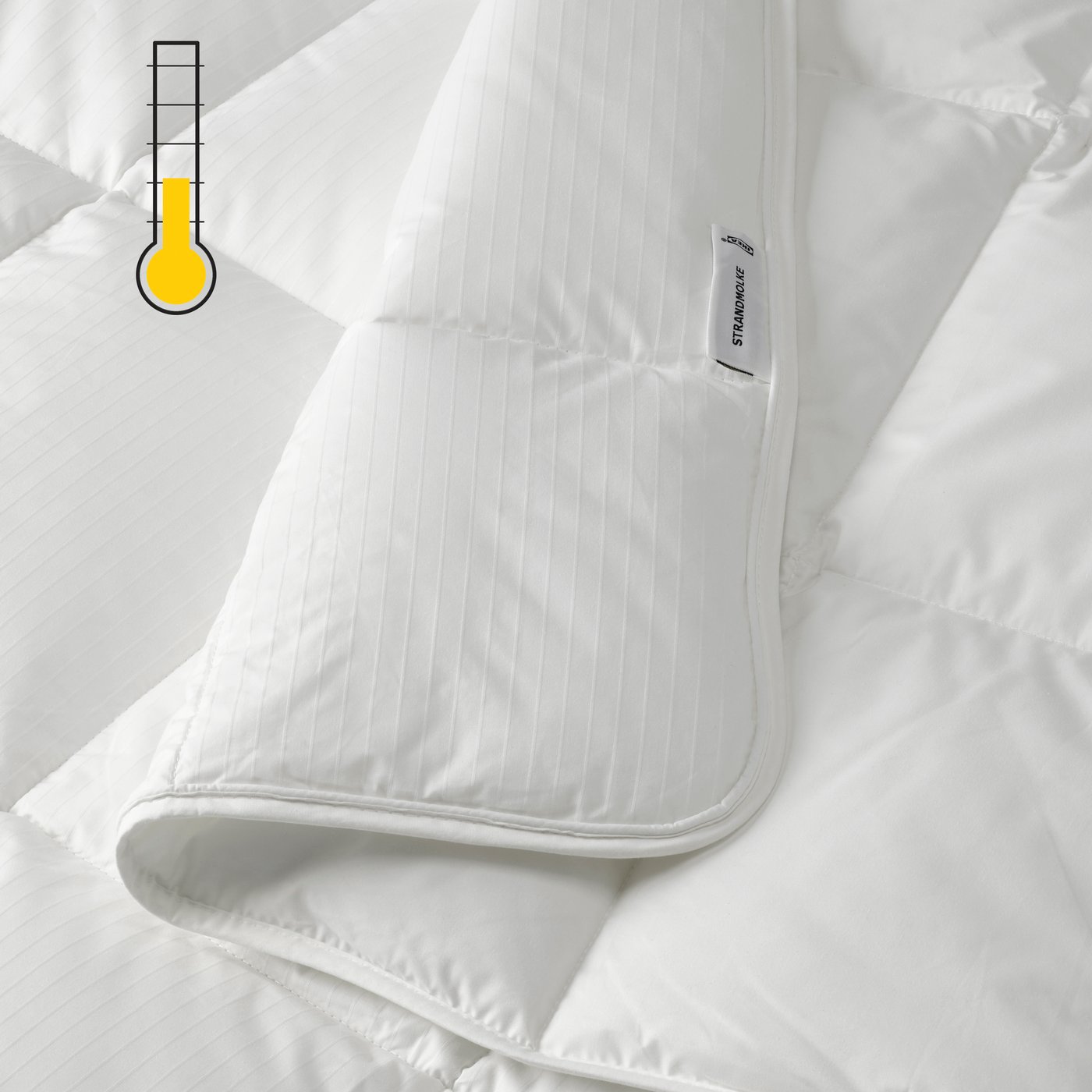 A close-up of a folded white duvet with a yellow light-warm temperature symbol in the top left corner.