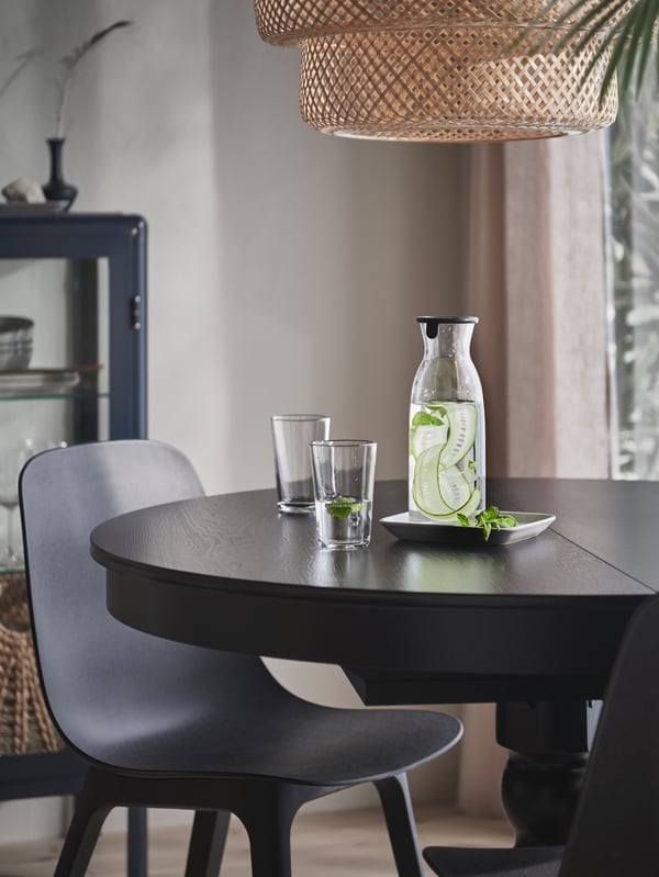 A dining area with a carafe and glasses on a black INGATORP extendable table, surrounded by anthracite ODGER chairs.